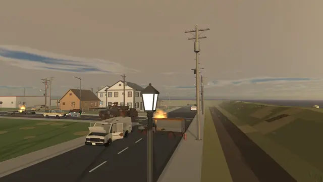 A road past burning wrecks toward a small town at dusk.